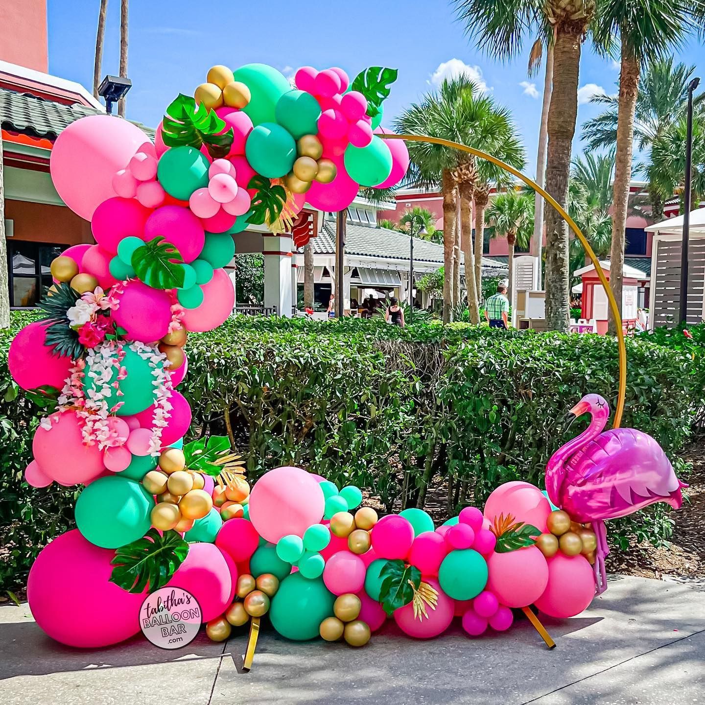 A bunch of pink and green balloons are sitting on the sidewalk.