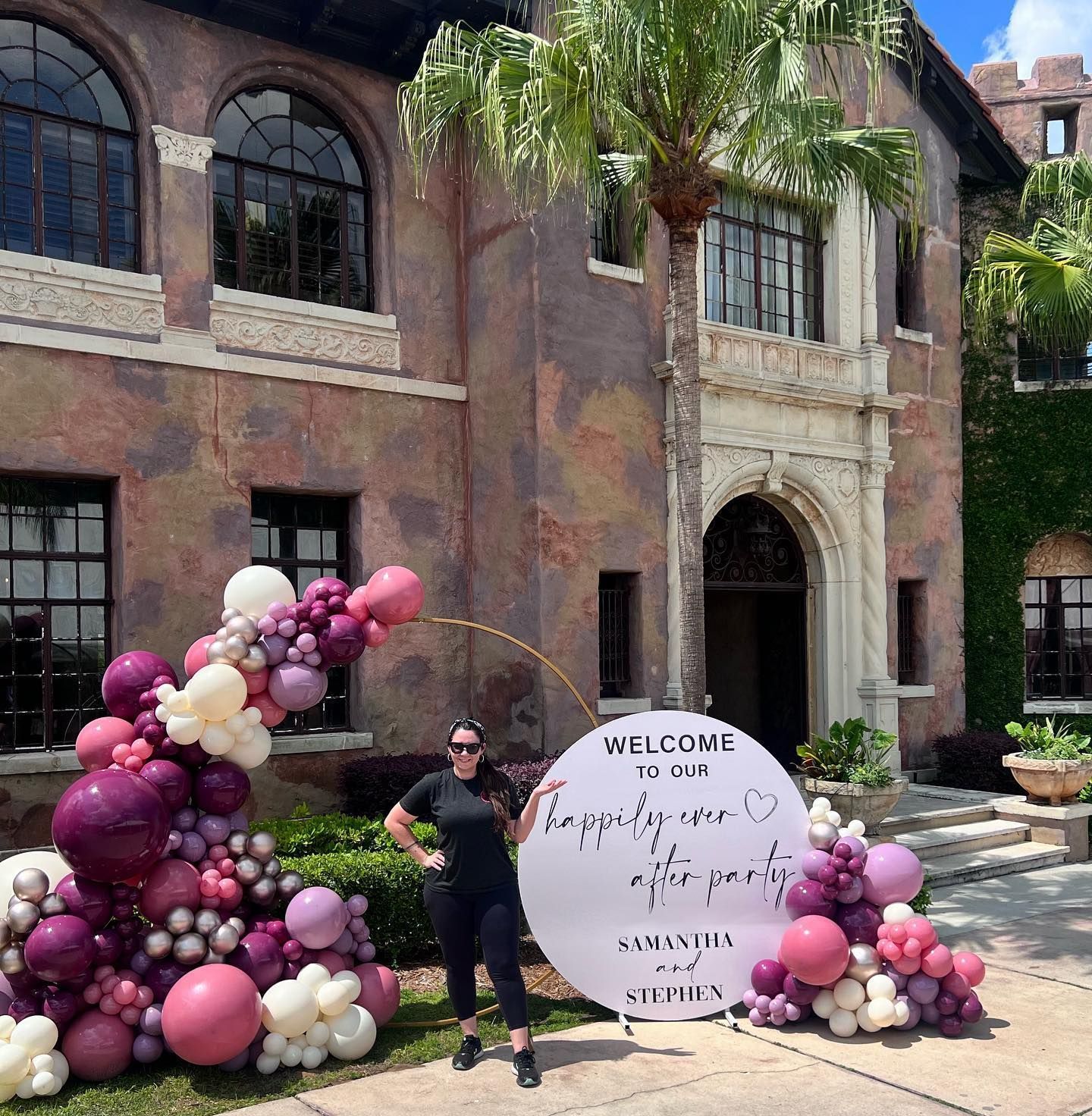 A woman is standing in front of a building with balloons and a welcome sign