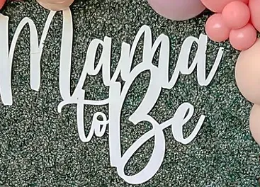 a sign that says `` mama to be '' is surrounded by pink balloons .