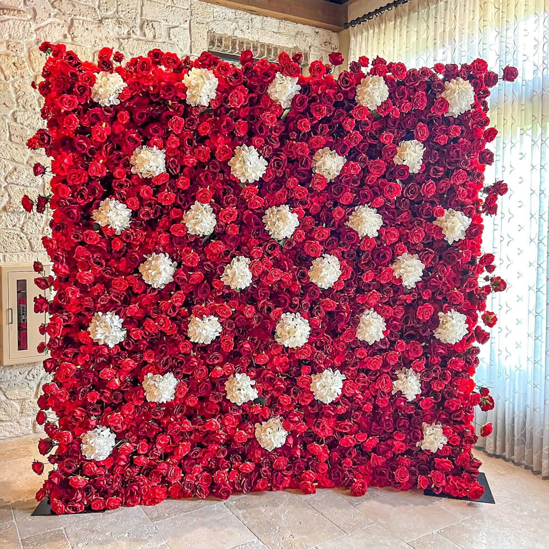 A wall of red roses and white pom poms in a room.