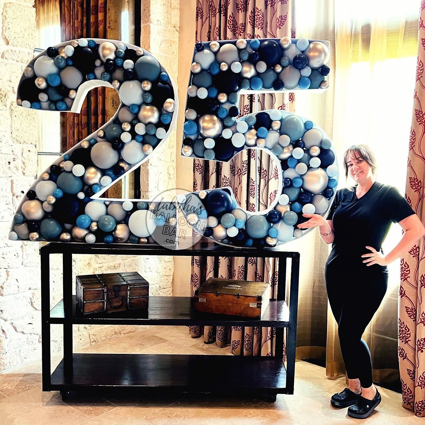 A woman is standing in front of a large number 25 made of balloons