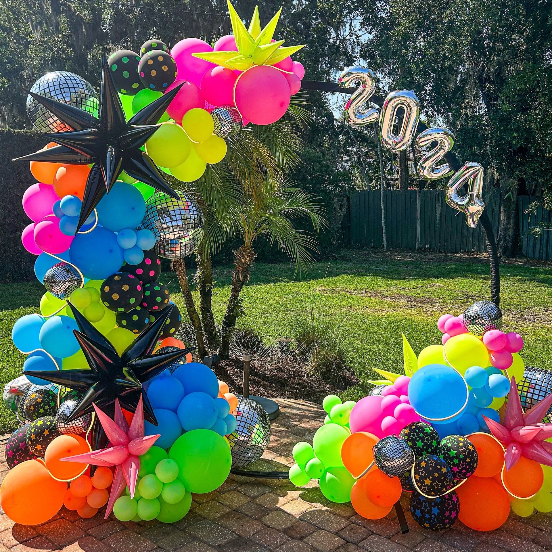 A bunch of colorful balloons are sitting on a brick sidewalk.
