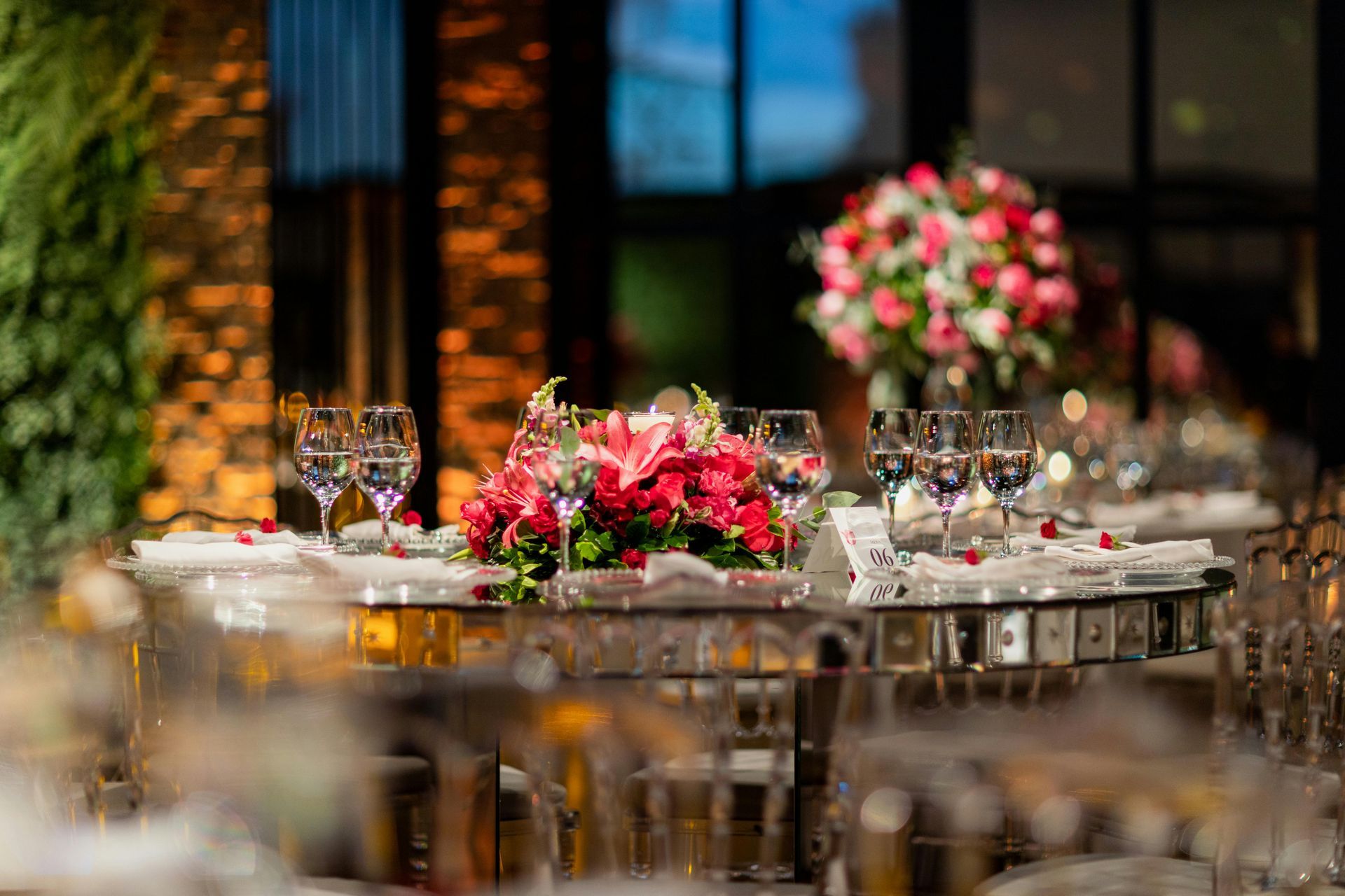 Elegant banquet table with red floral centerpieces, glassware, and candlelit decor in a softly blurred venue