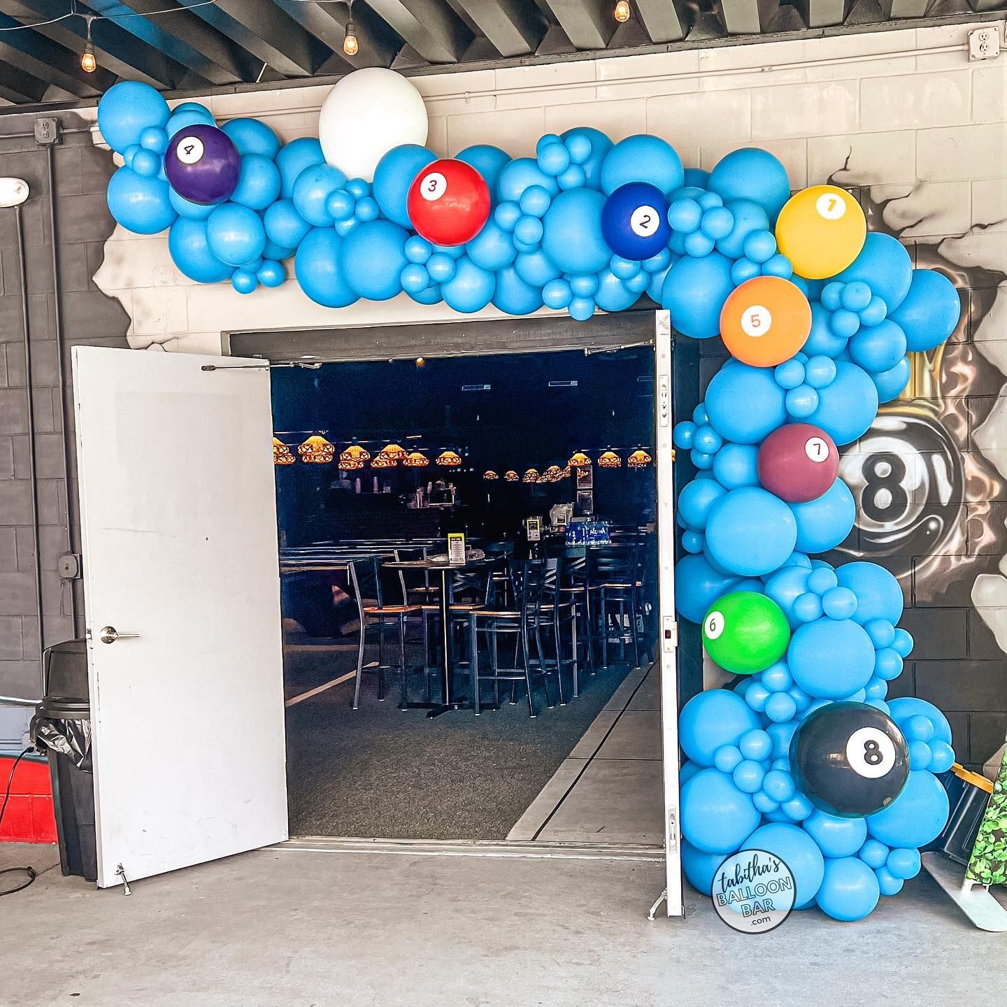 A doorway is decorated with blue balloons and pool balls.