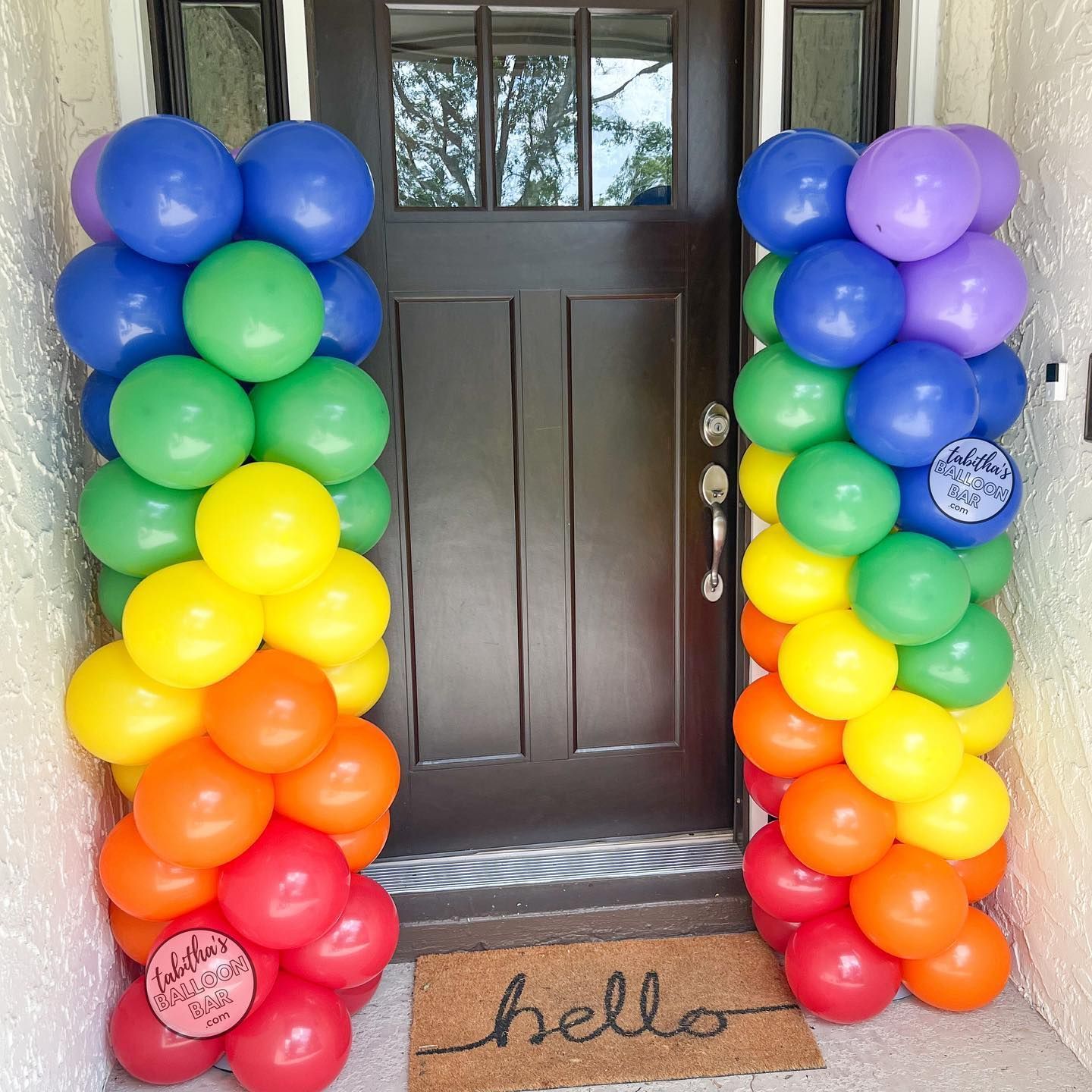 A door is decorated with rainbow colored balloons and a hello mat