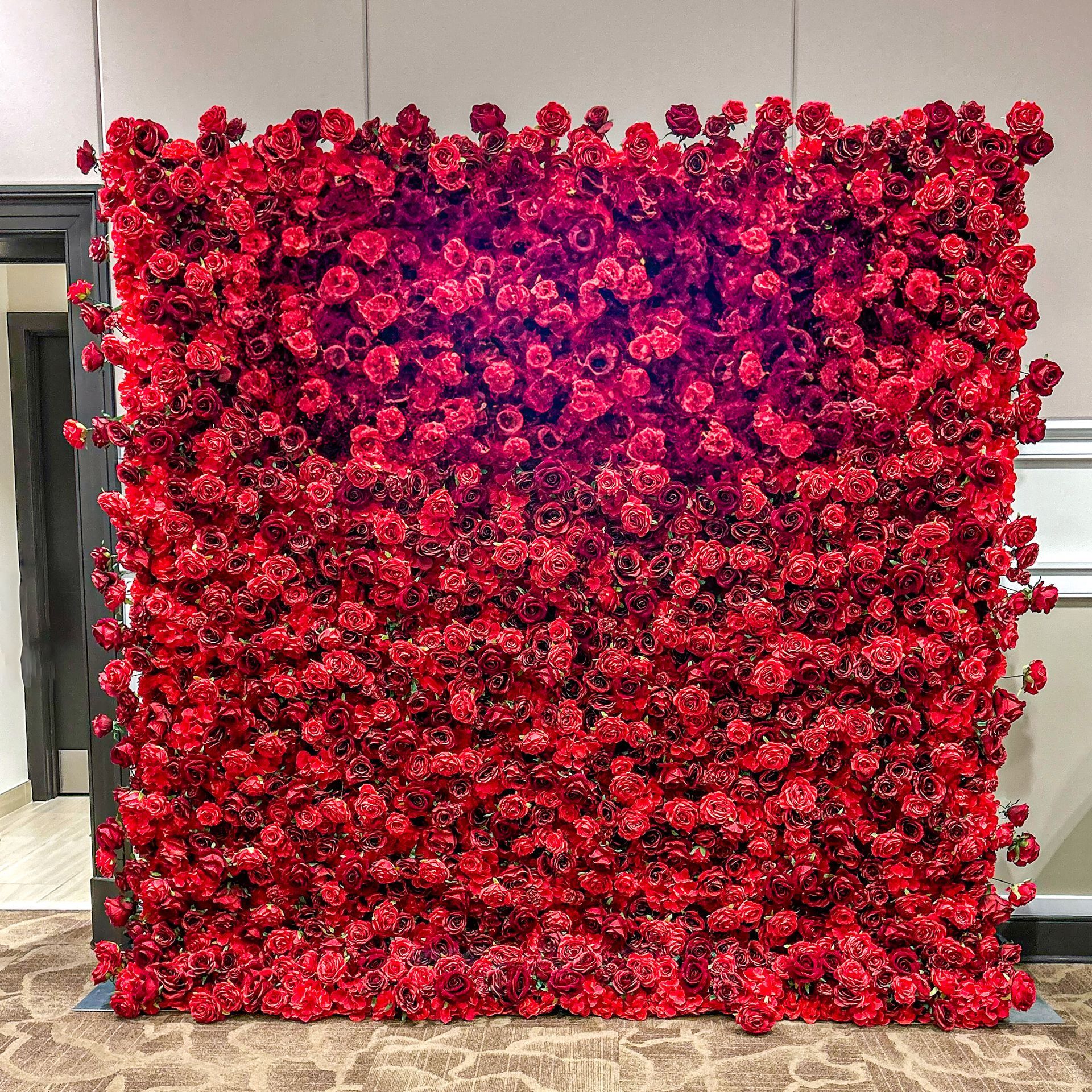 A wall covered in red roses in a room.