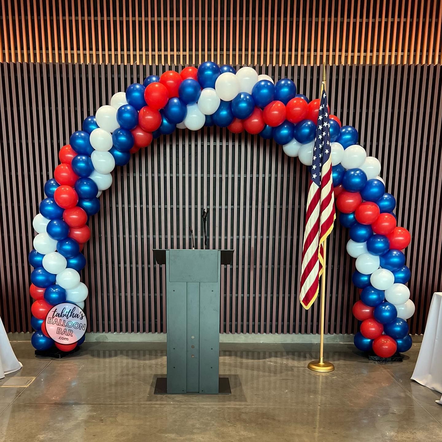 A podium is surrounded by red white and blue balloons