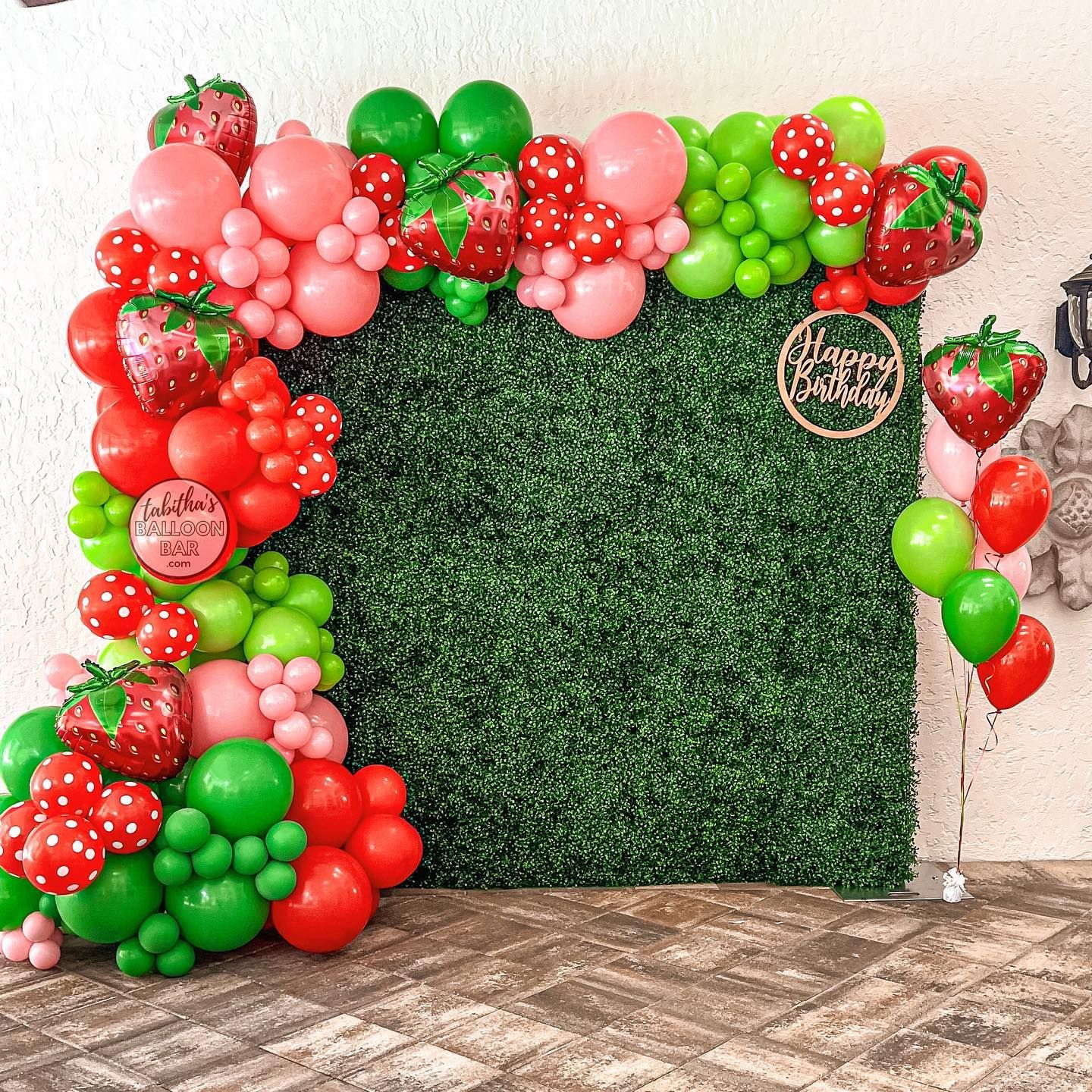 A bunch of balloons with strawberries on them are sitting on top of a green wall.
