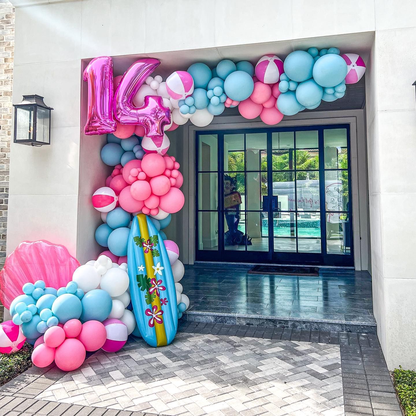 A surfboard is sitting in front of a door decorated with balloons.