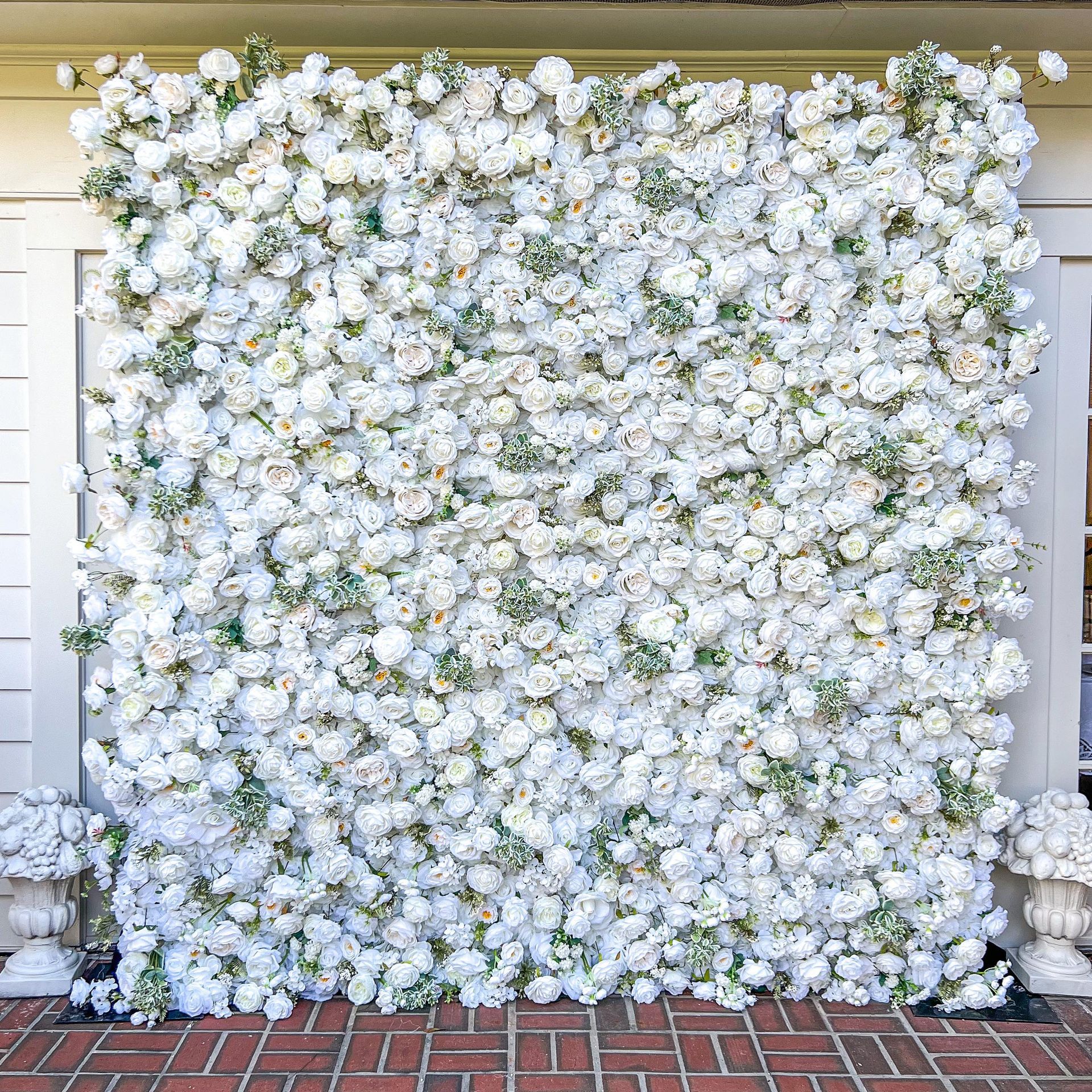 a wall of white flowers is sitting on a brick floor .