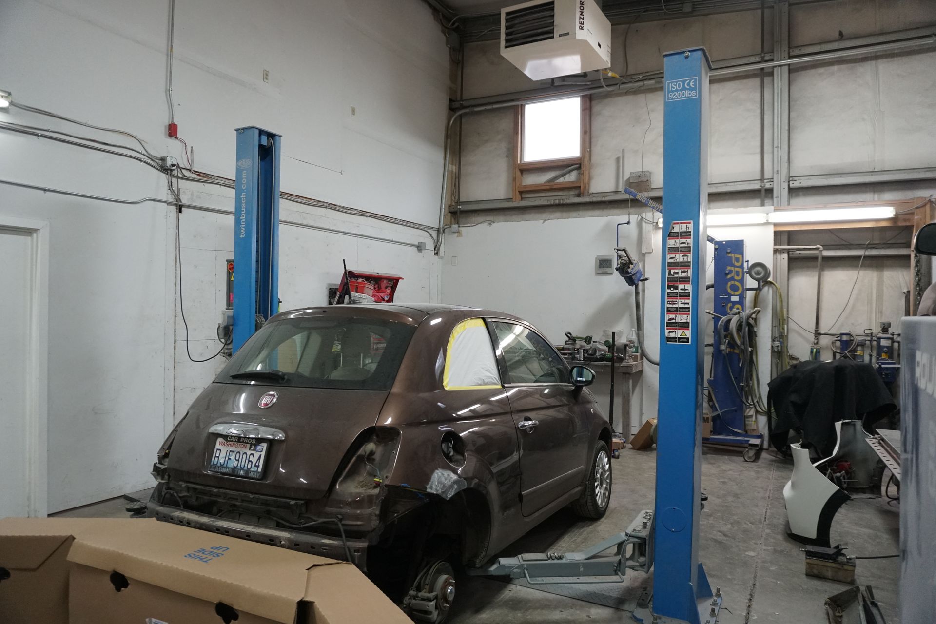 Person using power sander on white car panel in a repair shop.