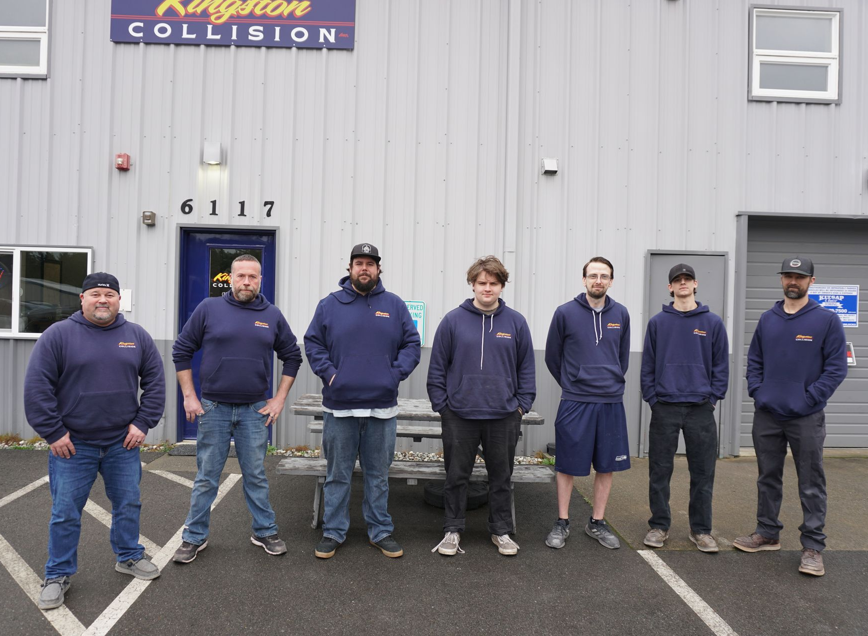 Person polishing black car with a yellow buffer; blue tape protects edges.
