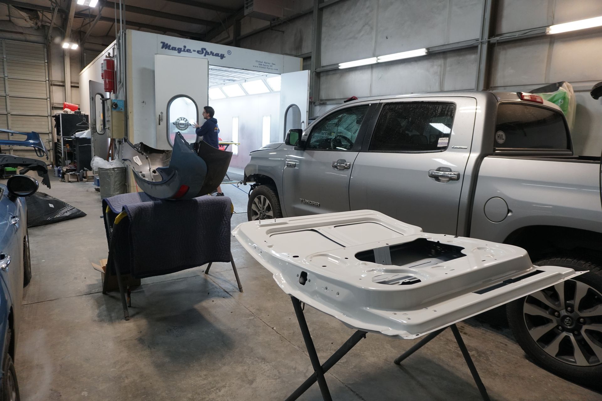 Person using a blue power sander on the rear of a red car, sanding down to the bare metal.