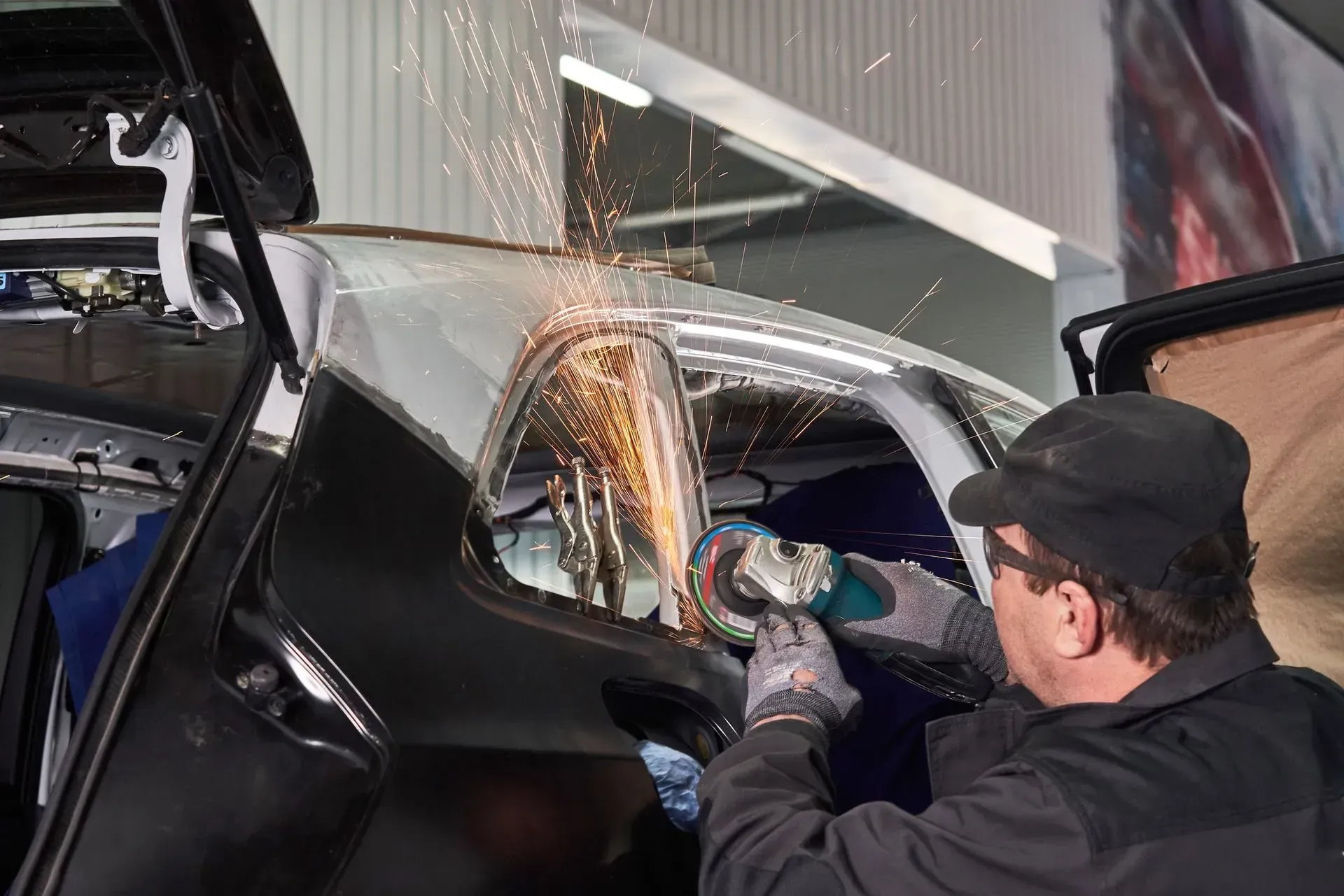 Man using a grinder on a car frame, producing sparks. Workshop setting, black car.