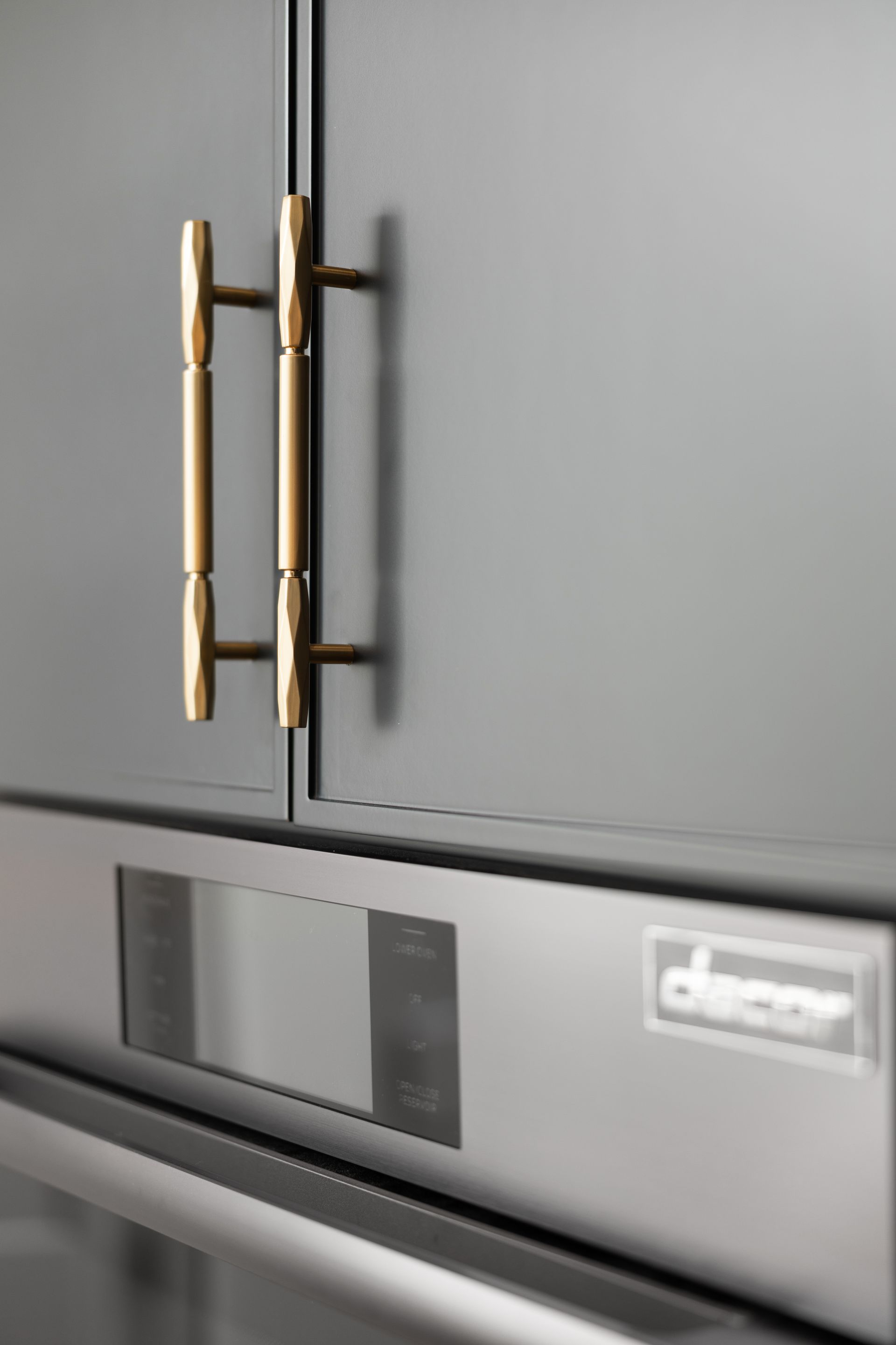Close-up of a dark gray cabinet with gold handles above a stainless steel oven.