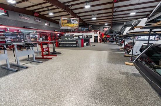 Large auto shop interior with vehicles, tools, and red metal work tables.
