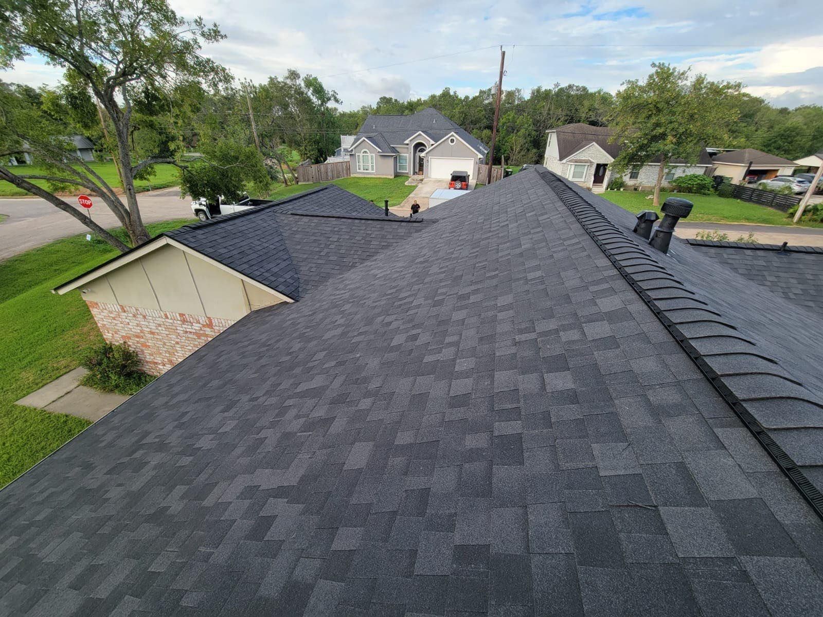 A newly shingled gray roof of a house with other houses and trees in the background.