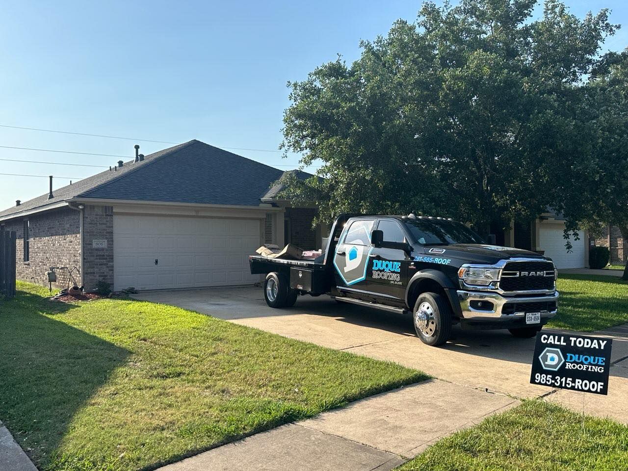 Black pickup truck parked in front of a house on a sunny day. Sign in front with phone number.