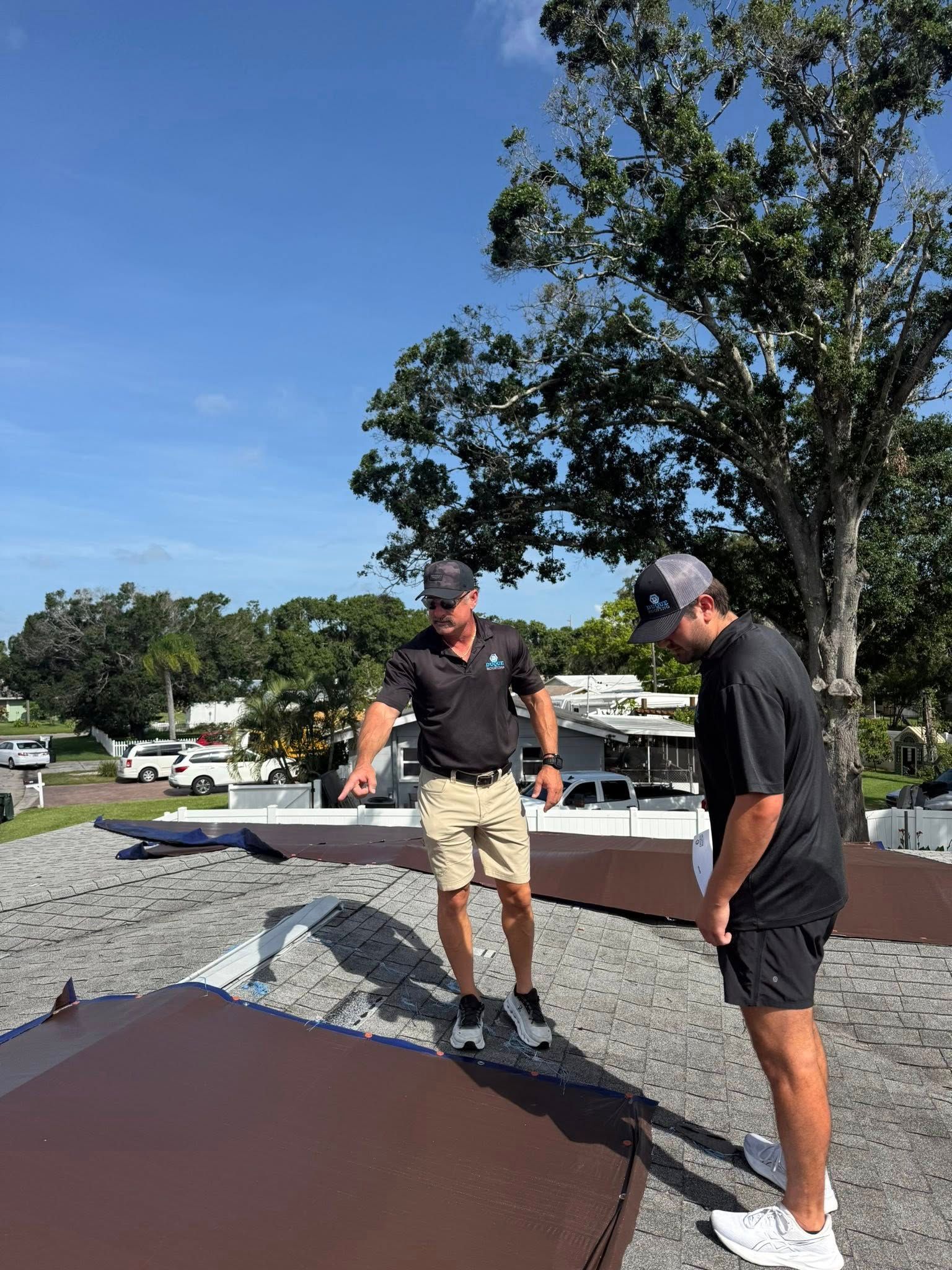 Two people on a rooftop examining brown metal panels. One points; blue sky background.