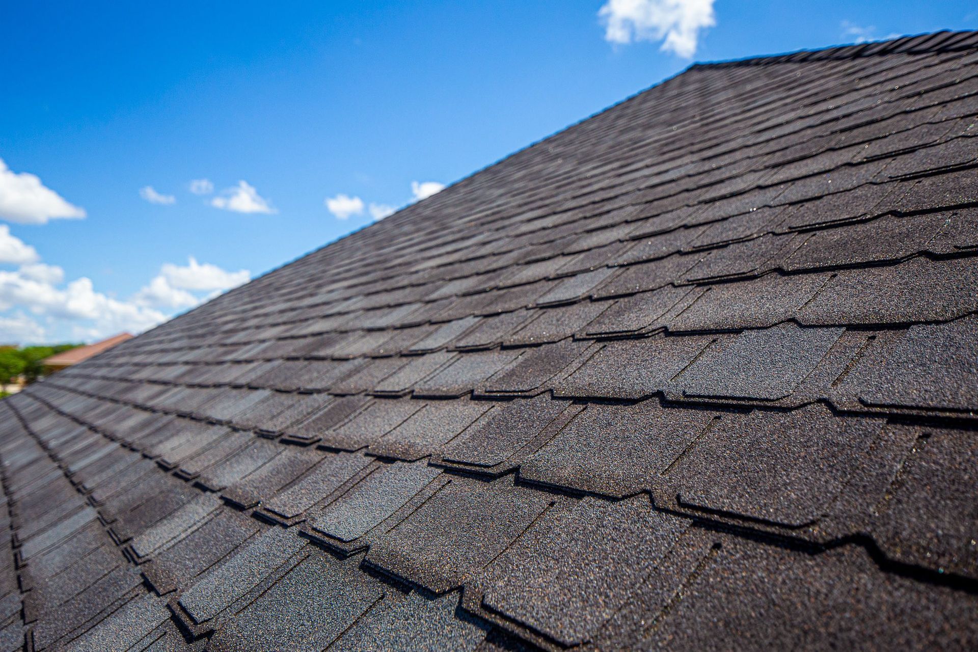 Dark gray composite roof tiles on a house under a blue sky with clouds.
