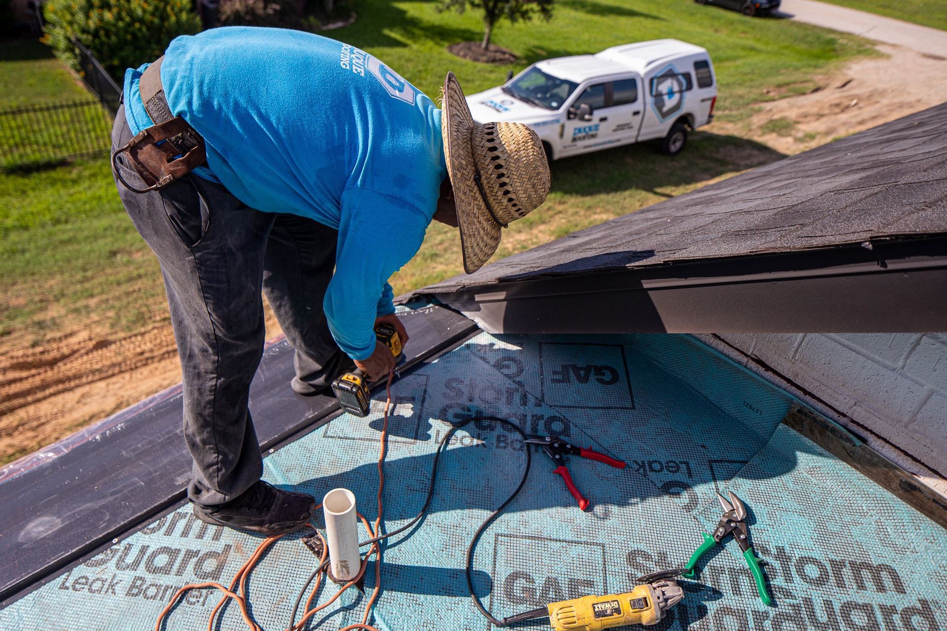 Roofer installing shingles on a roof. A white truck with a company logo is in the background.