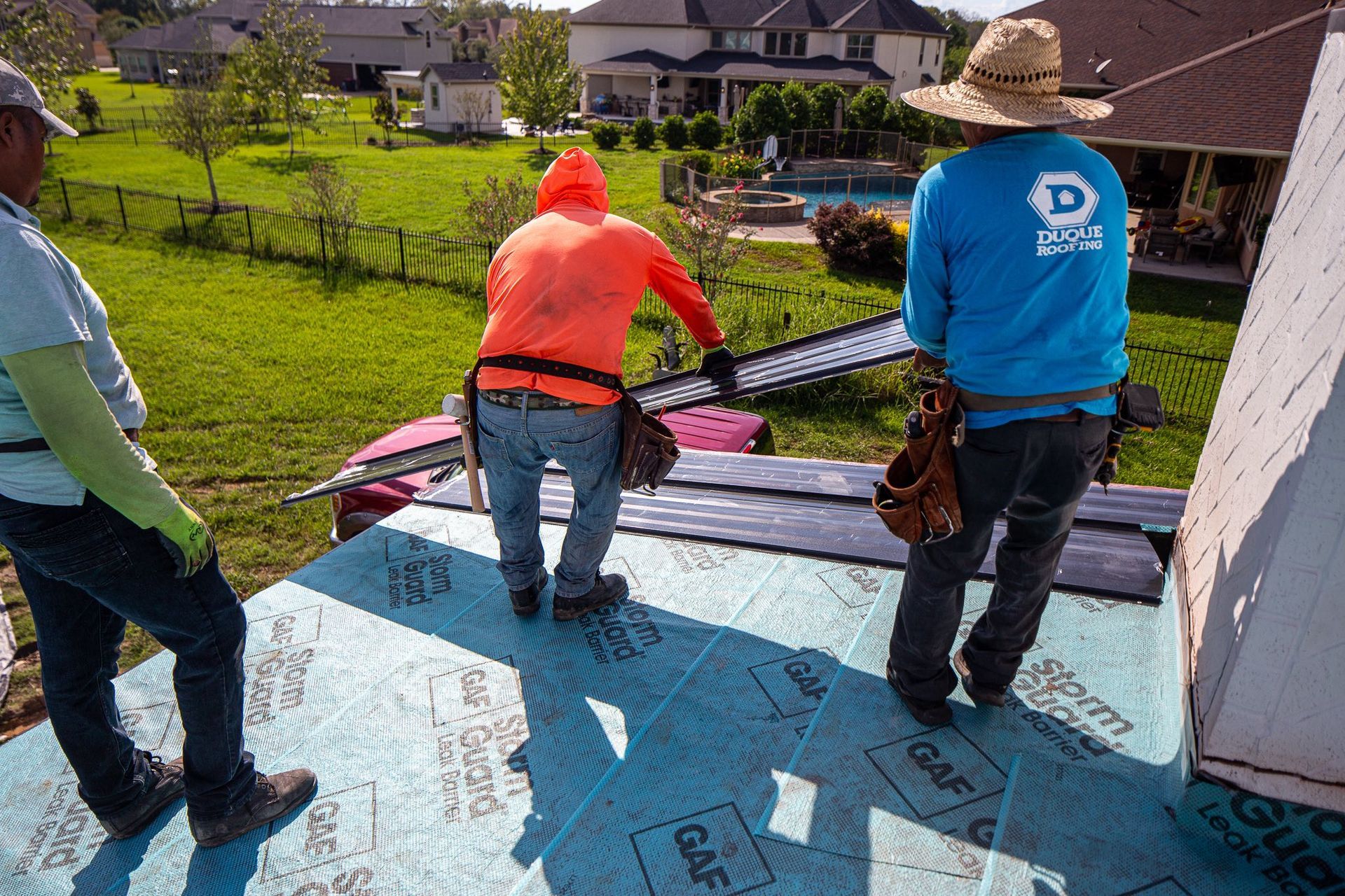 Three construction workers on a rooftop, installing roofing material. Sunny day.
