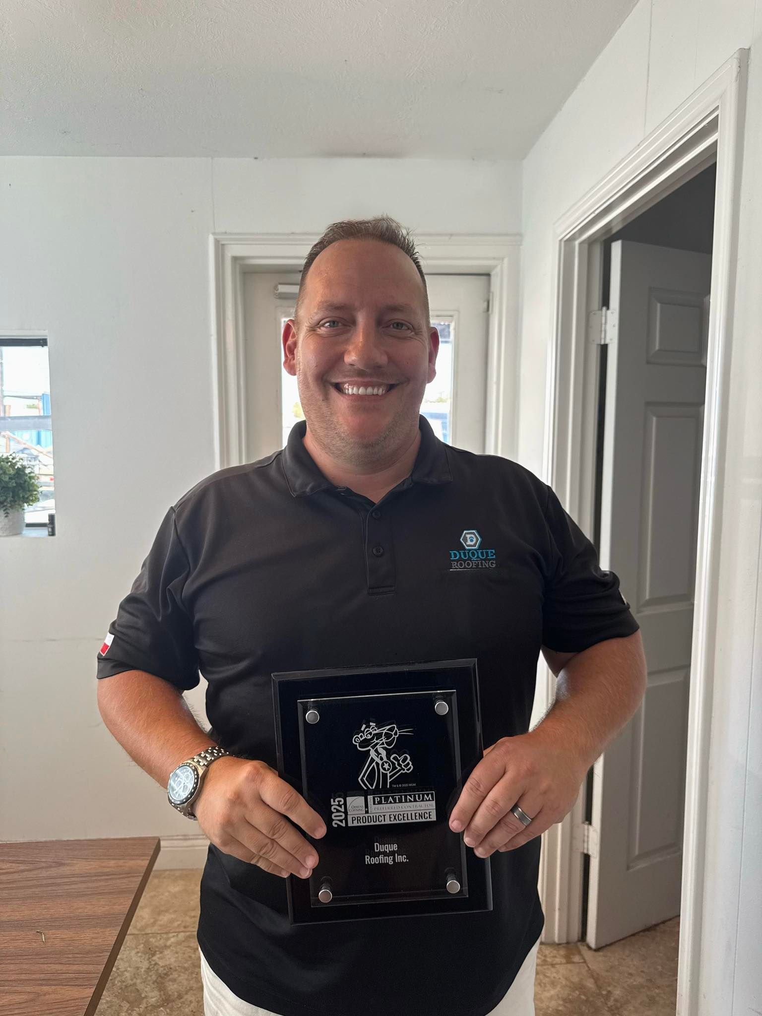 Man in black polo shirt holding an award, smiling indoors.
