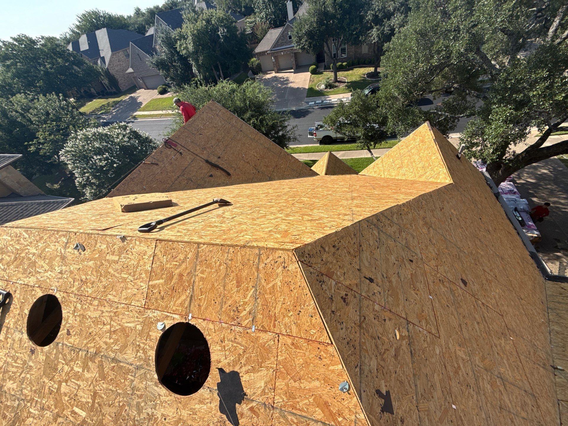 New roof construction with oriented strand board (OSB) and round holes, overlooking a neighborhood.