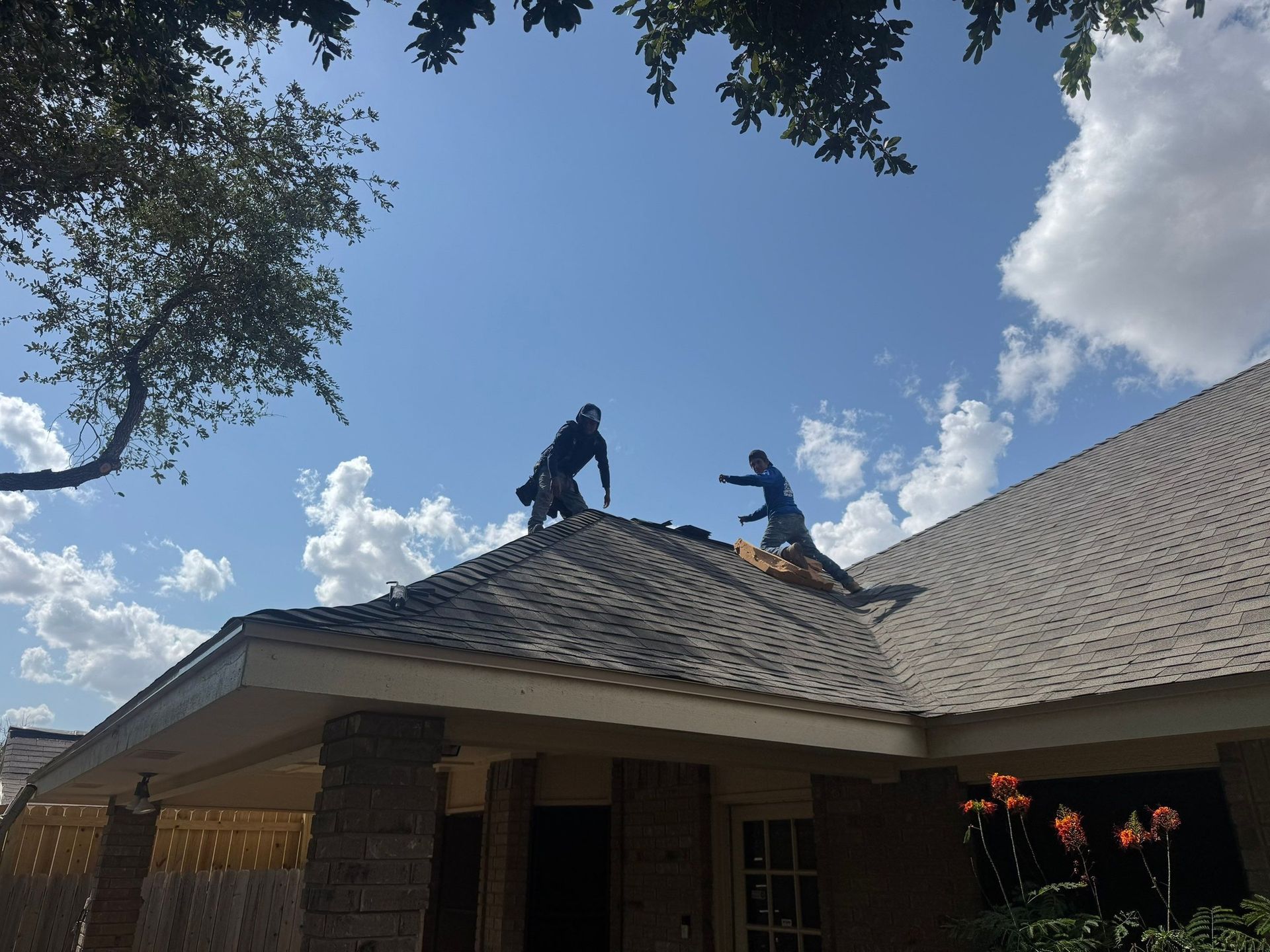 Two workers repairing a roof on a sunny day with clouds.