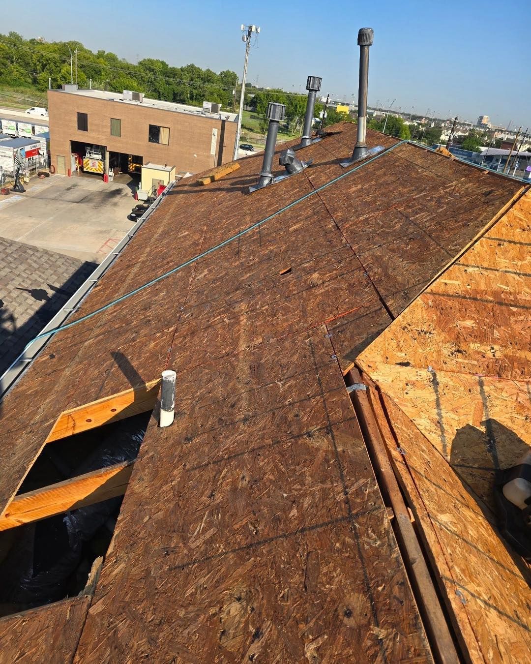 Rooftop with chimneys and unfinished brown wood panels, building and cityscape in the background.