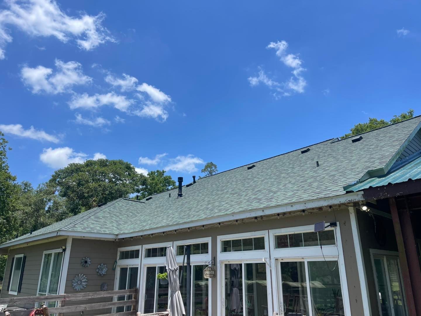 Low-angle view of a house with a green roof against a bright blue sky with puffy clouds.
