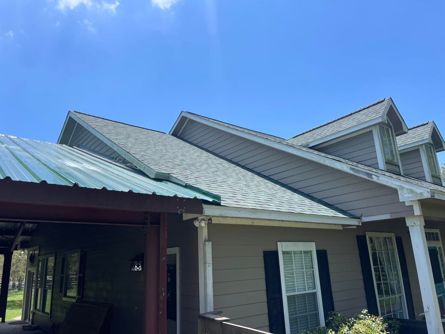 House with a gray shingled roof, green metal awning, and blue sky.