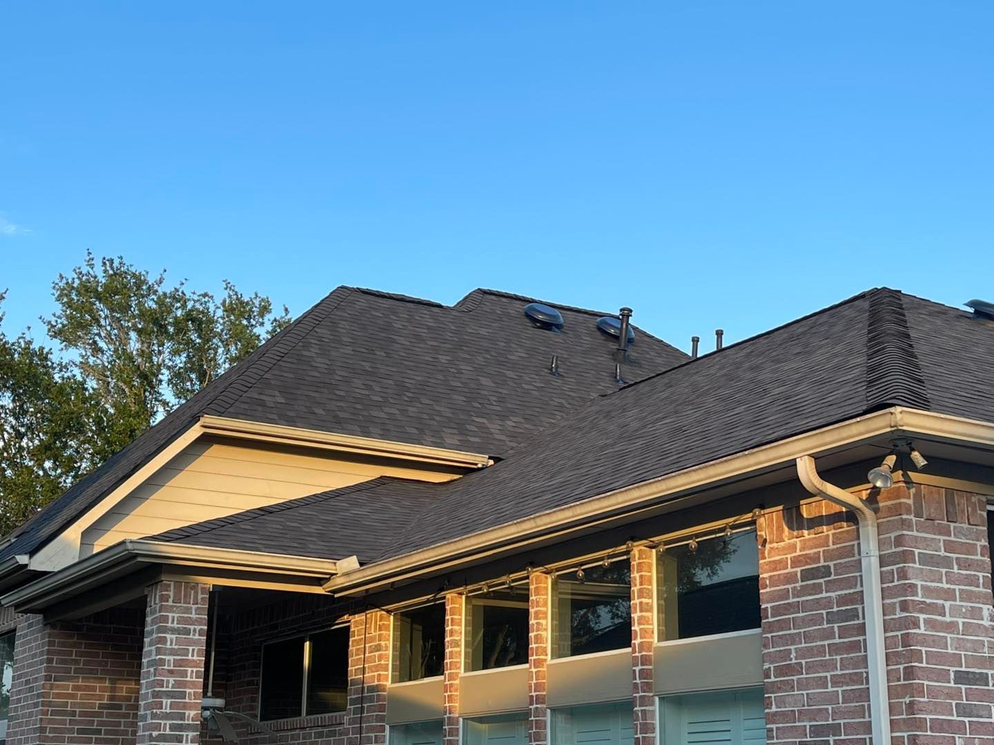 Dark shingle roof on a brick and beige house, with clear blue sky.
