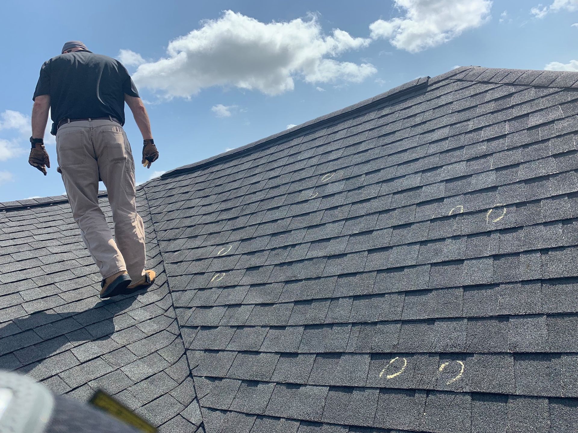 Person walking on a dark shingled roof under a partly cloudy sky.