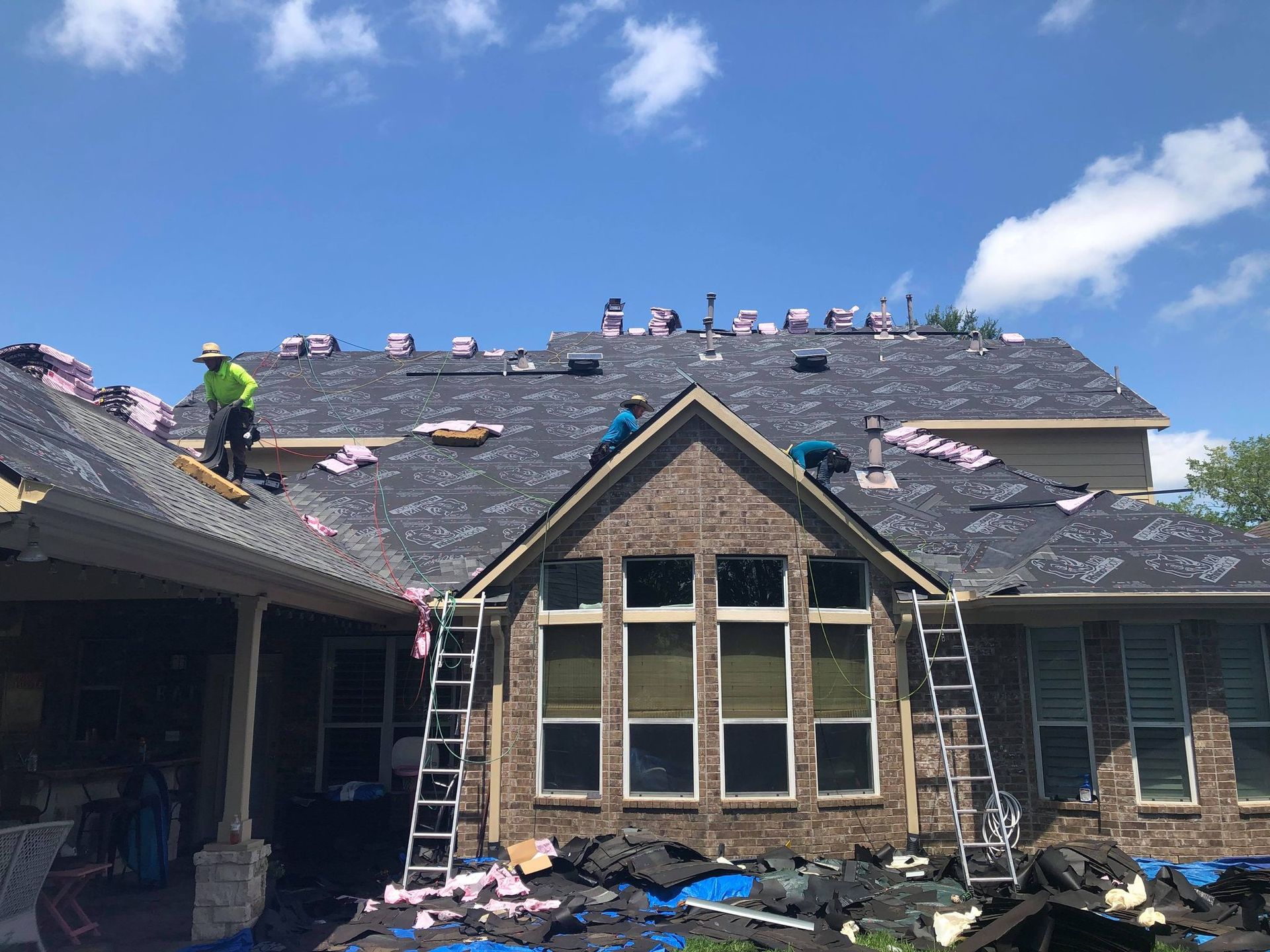 Roofers working on a brick house roof under a clear blue sky.