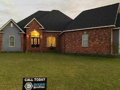 Brick house with a dark roof and a sign in the front yard that says “Call Today.”