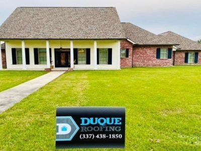 House with brown roof, green lawn, and Duque Roofing sign. (337) 438-1850.