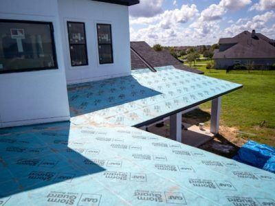 A house under construction with blue roof underlayment; sunny outdoor setting.