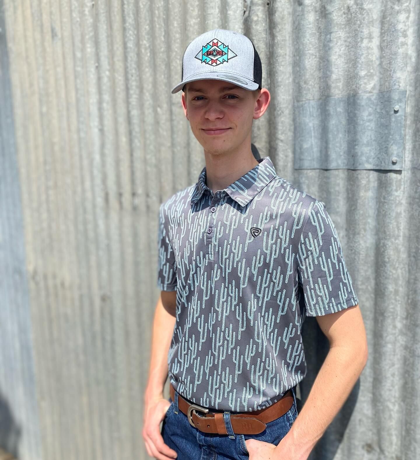 A young man wearing a hat and a polo shirt is standing in front of a metal wall.