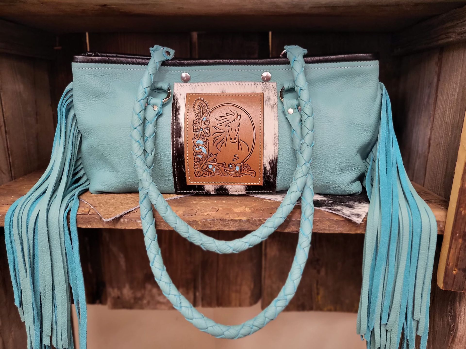 A turquoise purse with fringe is sitting on a wooden shelf.