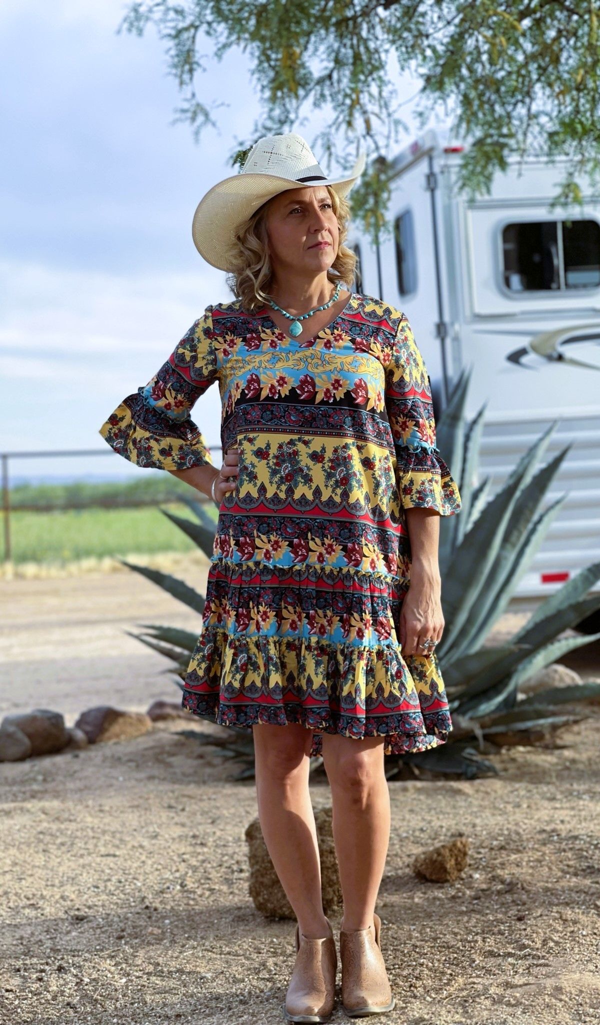 A woman wearing a cowboy hat and a dress is standing in front of a trailer.