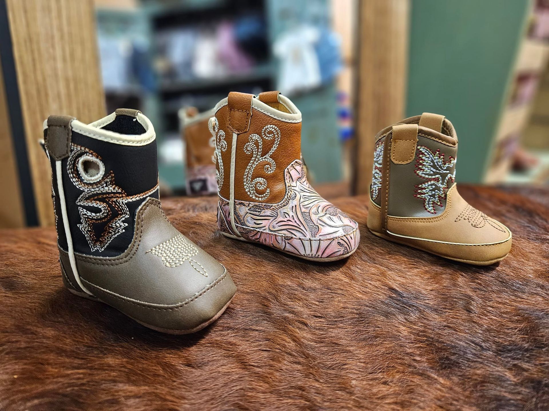 Three baby cowboy boots are sitting on top of a brown rug.