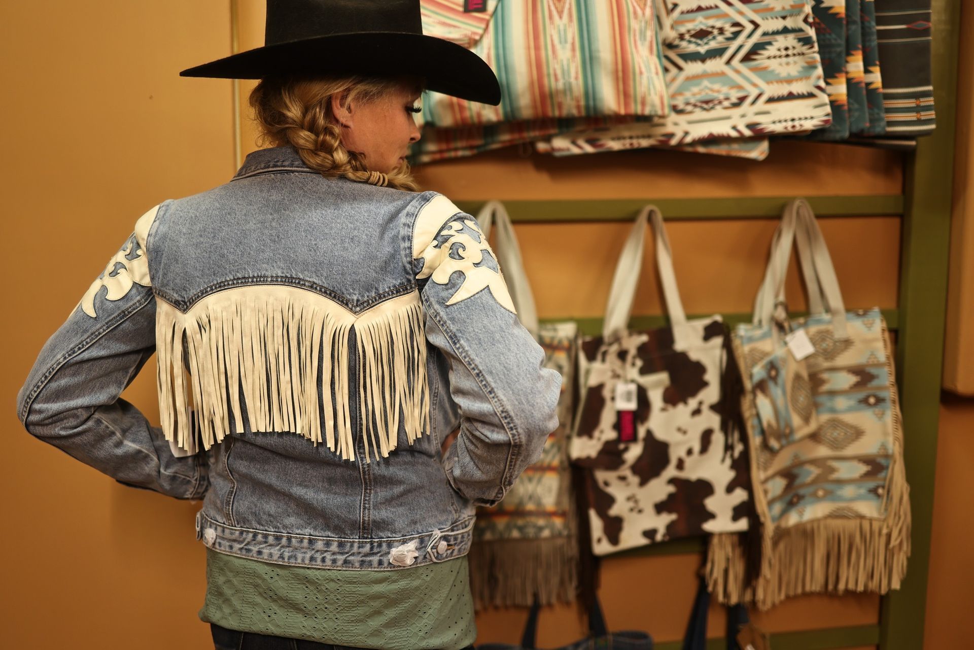 A woman wearing a cowboy hat and a denim jacket with fringe
