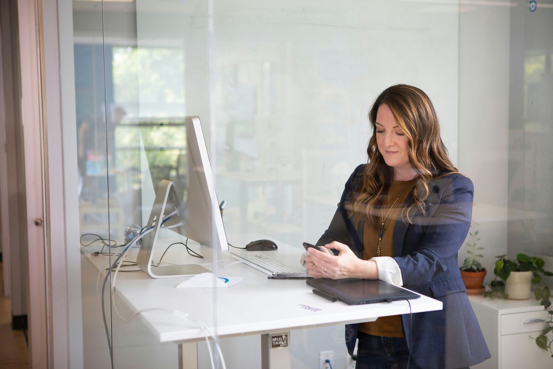 A woman is standing at a standing desk in front of a computer.