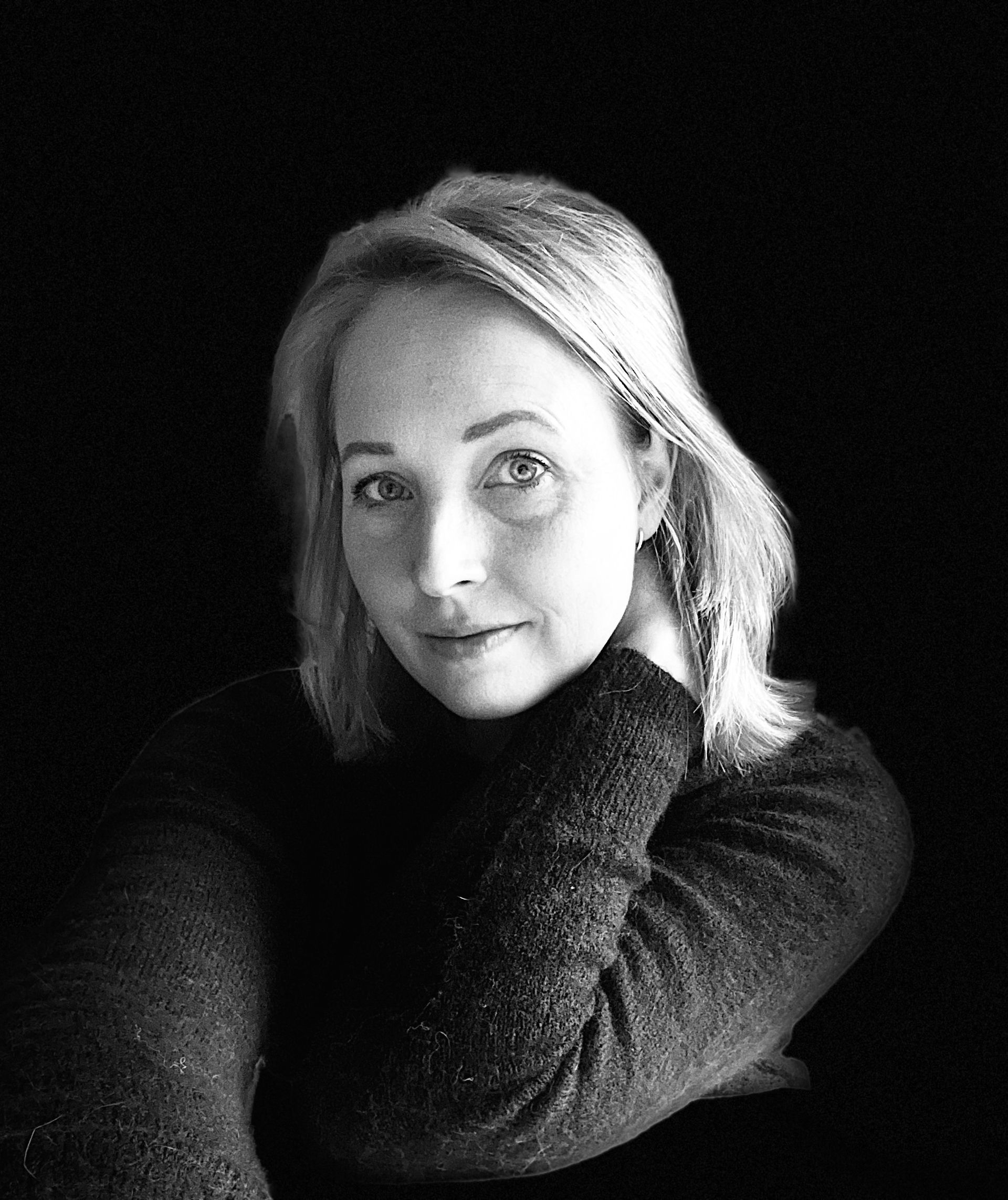 Zwart-wit portret van een persoon met licht haar, die zijn hoofd op een hand laat rusten tegen een donkere achtergrond.