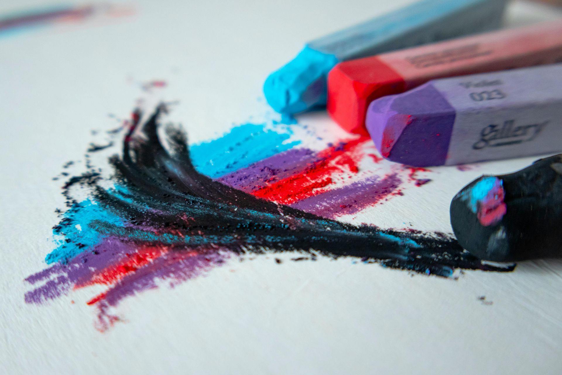 Kleurrijke pastelkrijtjes op wit papier met zwarte en magenta vlekken en poederstrepen.