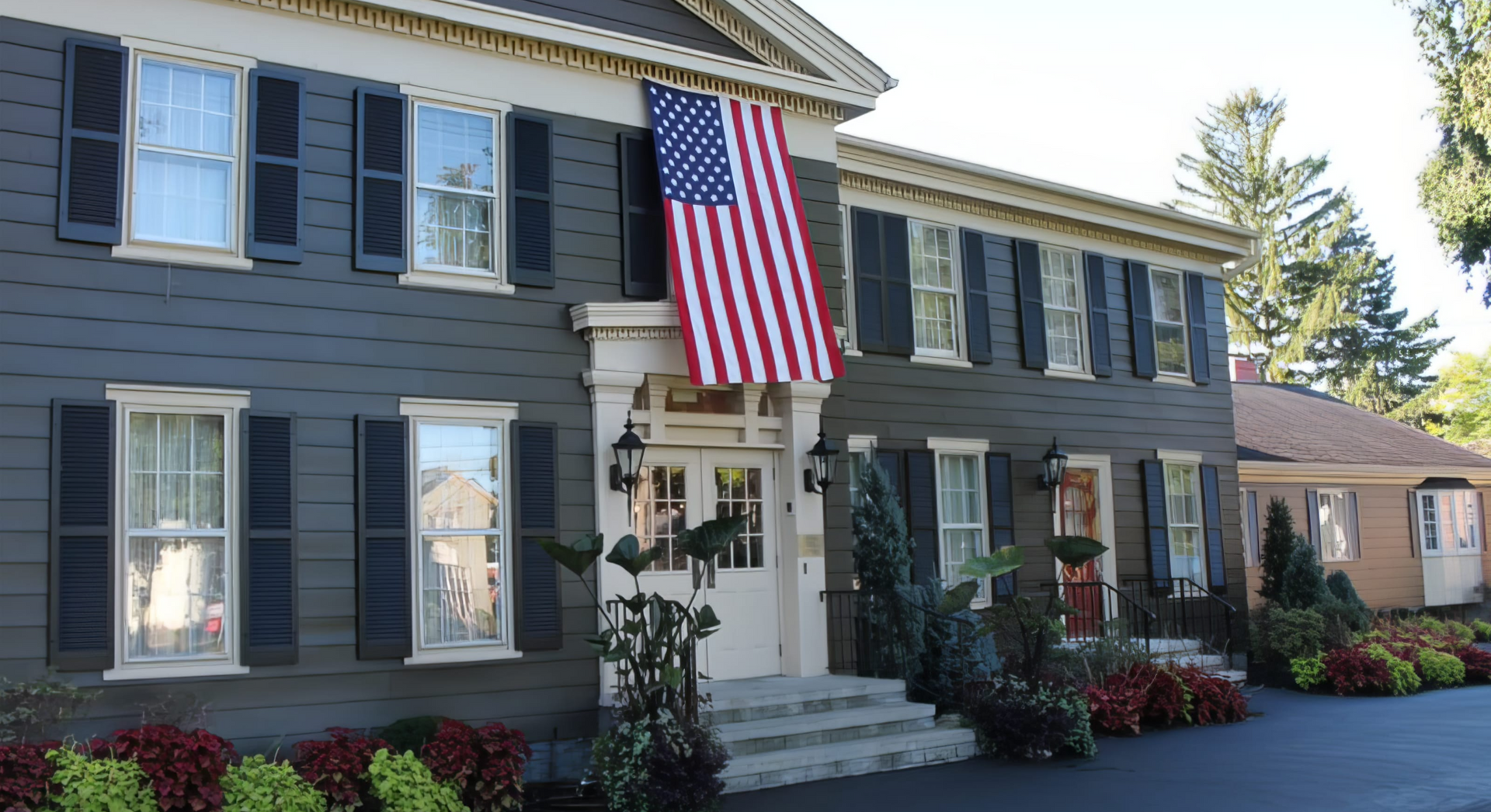 A large house with black shutters and an american flag