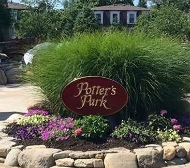A sign for potter 's park is surrounded by flowers and rocks.