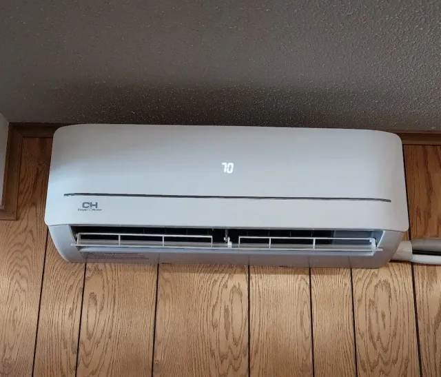 White ductless mini-split AC unit mounted on wood-paneled wall, displaying a 70-degree setting.