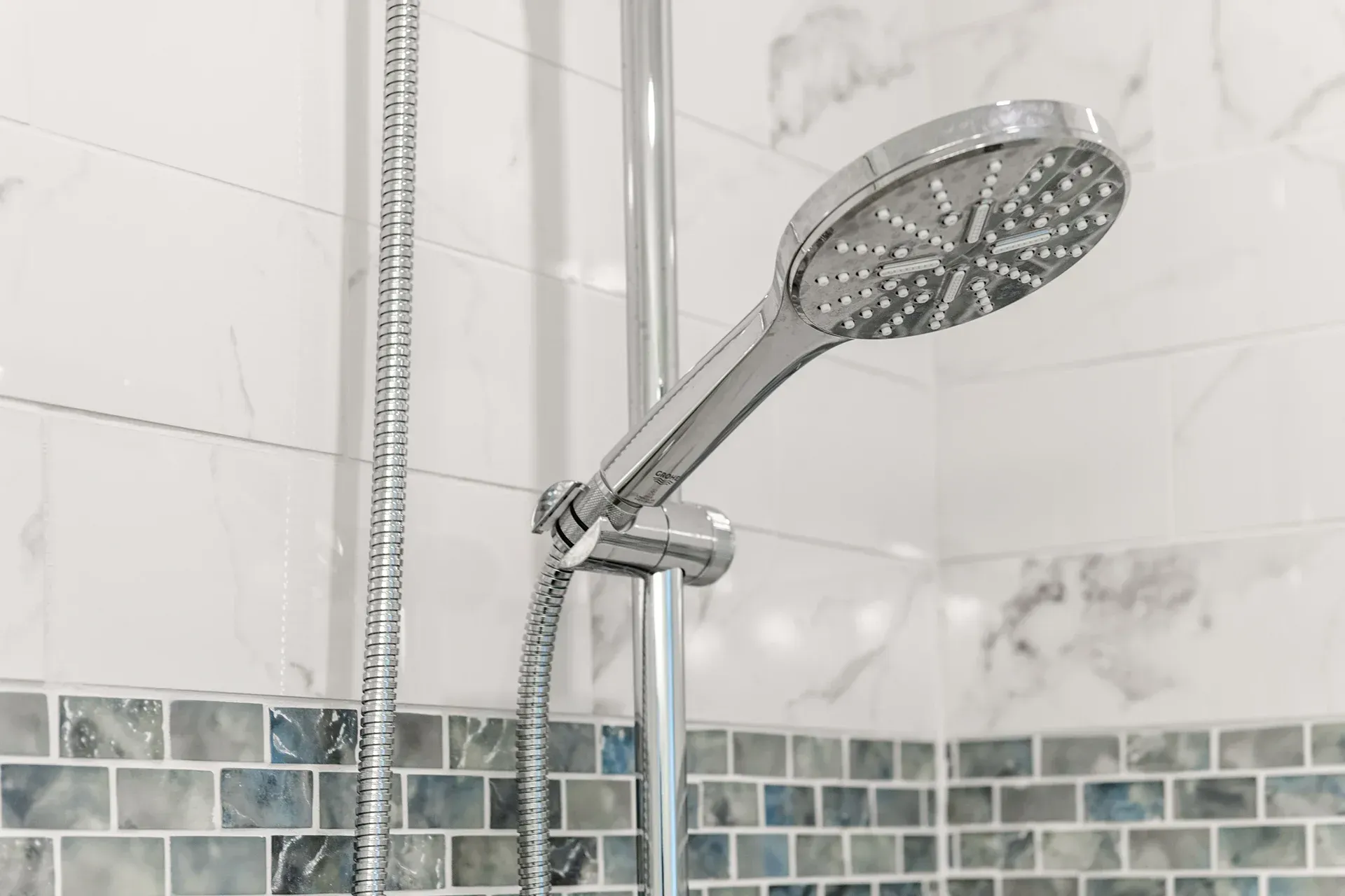 Silver shower head and hose against marble and mosaic tile wall.